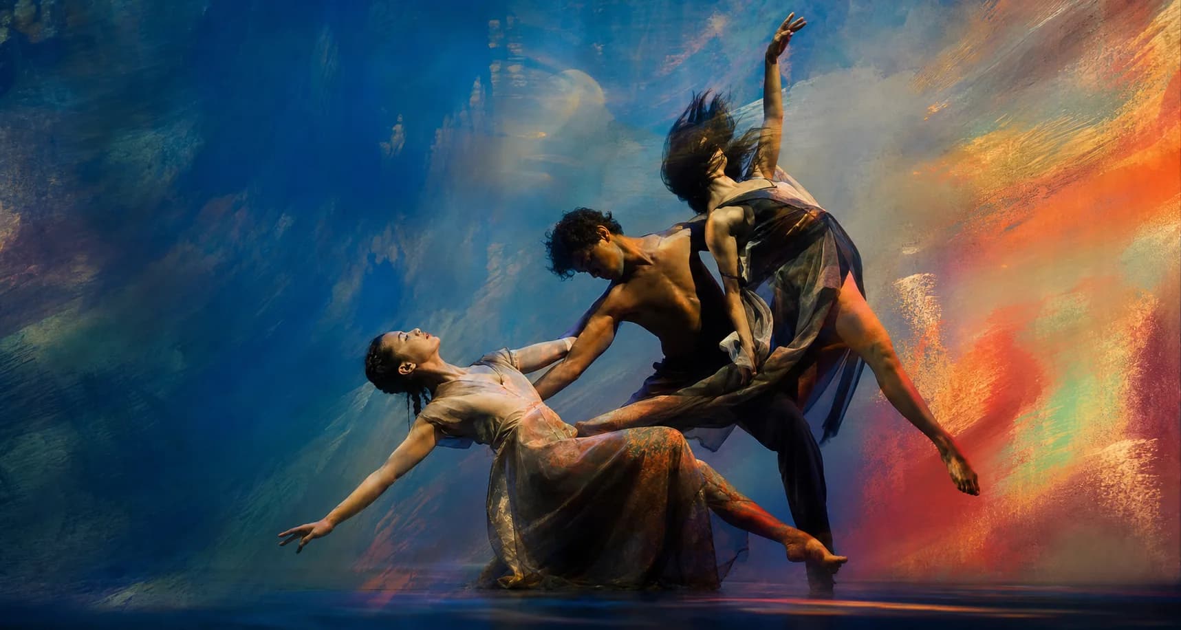 Three dancers in a sculptural formation against projected cobalt and vermilion color