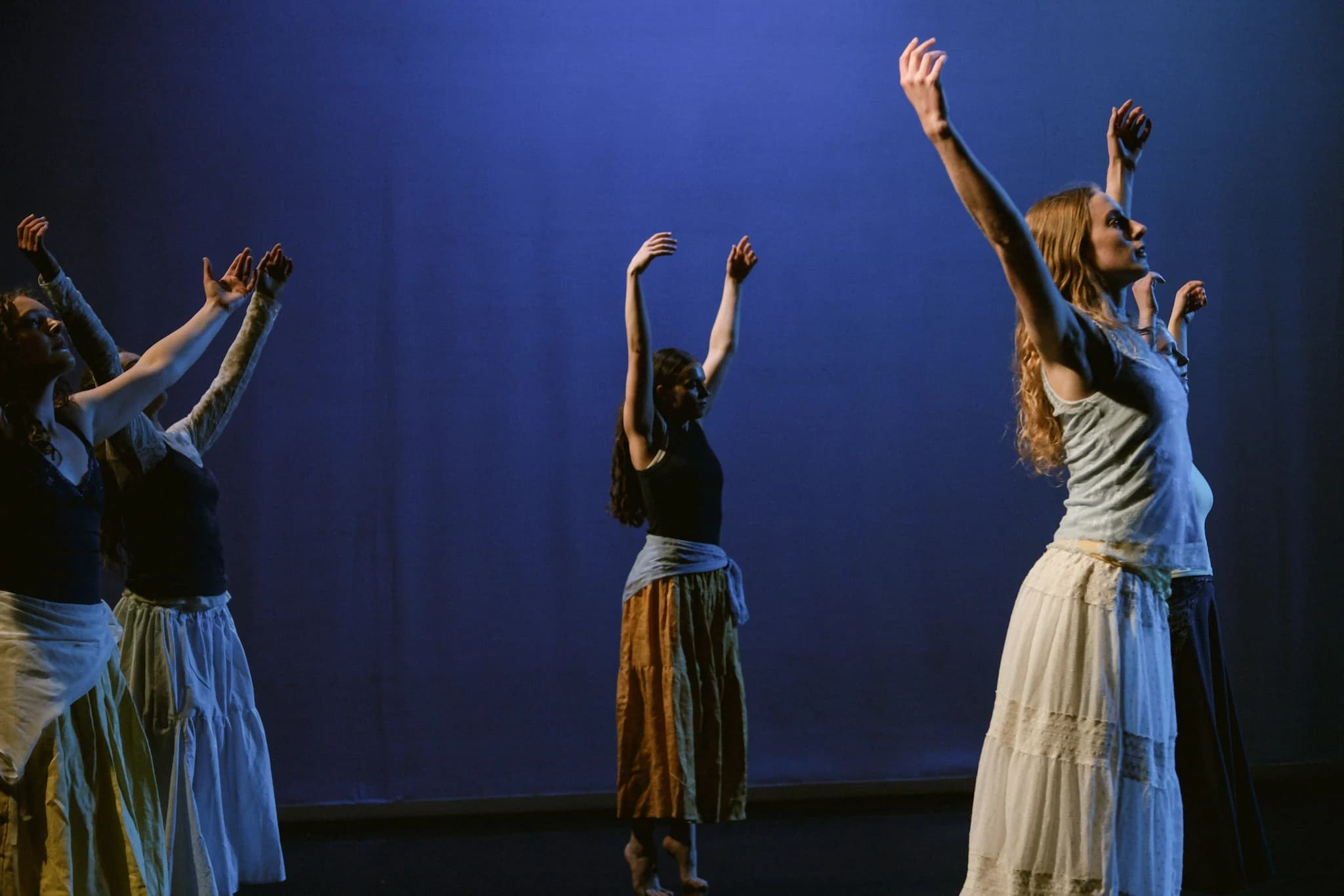 Eleven Stars dancers reaching upward beneath cobalt stage light