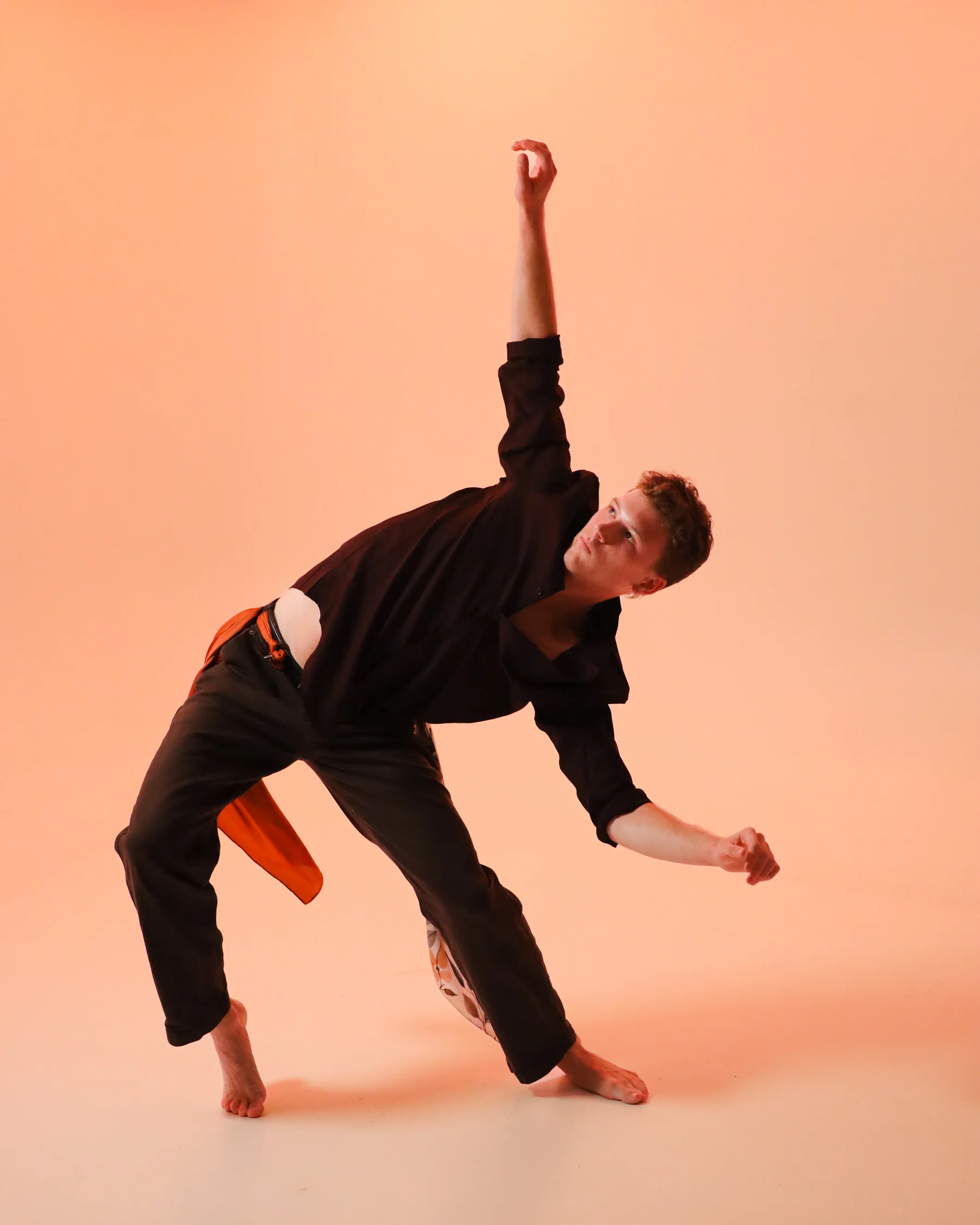 A dancer lunging with one arm reaching vertically toward the light