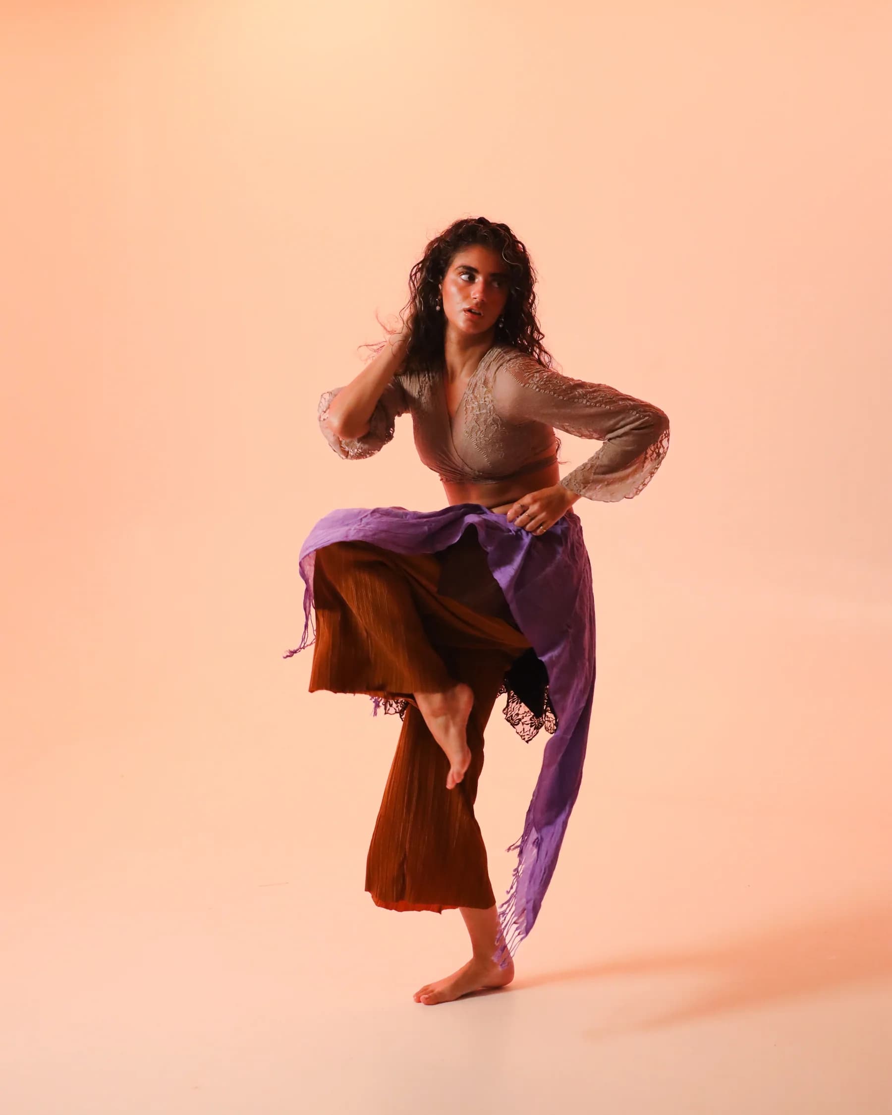 A dancer lifting one knee and wrapping her arms around a flowing purple skirt